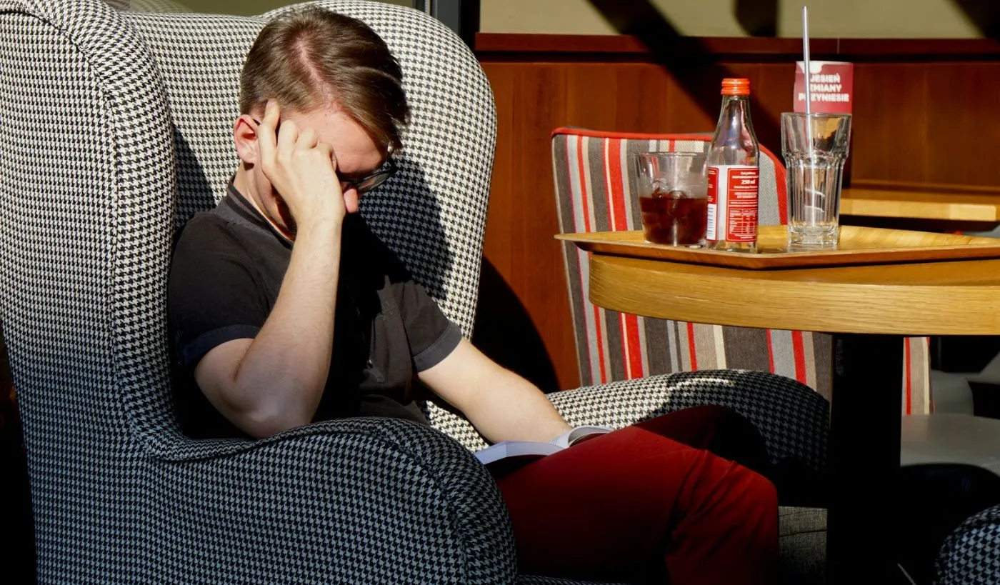 Młody mężczyzna siedzący w fotelu i czytający książkę biznesową, skupiony na lekturze i refleksji nad rozwojem osobistym oraz karierą zawodową