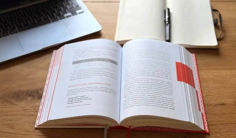 Otwarta książka biznesowa na biurku obok laptopa i notesu, symbol praktycznego czytania książek biznesowych i pracy z wiedzą