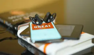 Audiobook na smartfonie ze słuchawkami na tle książek papierowych, audiobooki vs książki papierowe w rozwoju osobistym